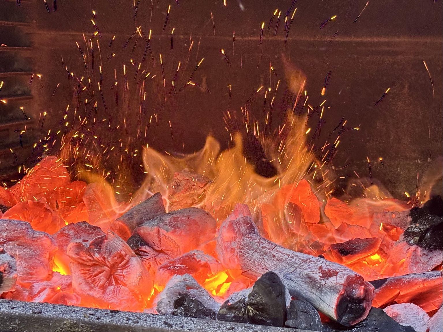 Brasa de carbón encendida con llamas y chispas en la parrilla de El Bejeque